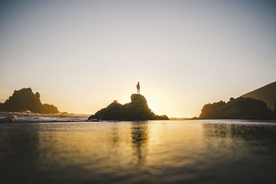 Distant view of person standing on rock formation against clear sky during sunset person