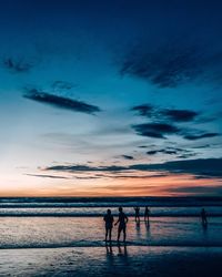 Silhouette people at beach against sky during sunset