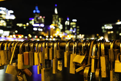 Close-up of padlocks on railing against illuminated city at night