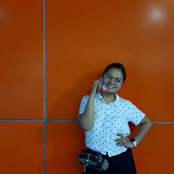 Portrait of a smiling young woman standing against wall