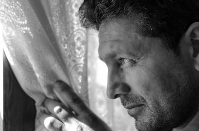 Close-up of thoughtful man looking away by curtain