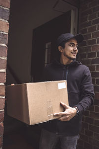 Delivery man with package looking away while standing at doorstep