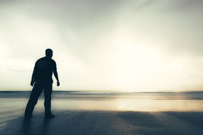 Rear view of silhouette man standing on beach against sky