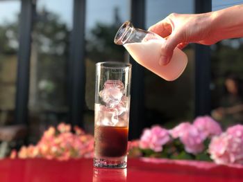 Cropped hand pouring milk in iced coffee on table