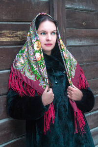 Woman wearing scarf standing against wooden wall