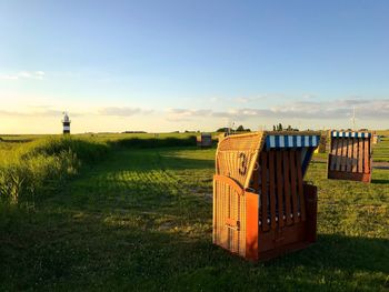 Hooded chairs on field against sky during sunset