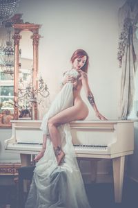 Side view of naked woman sitting on piano at home