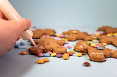 Cropped hand decorating gingerbread man cookies with blue background