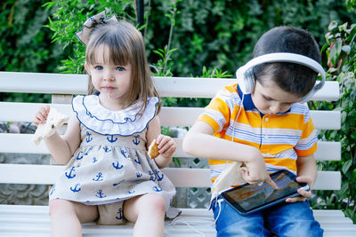 Cute boy listening music with sister on bench