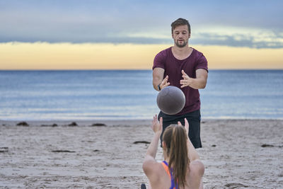 Young woman exercising with fitness instructor at beach