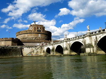 Arch bridge over river by buildings against sky