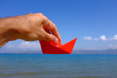 Cropped hand holding paper boat above sea