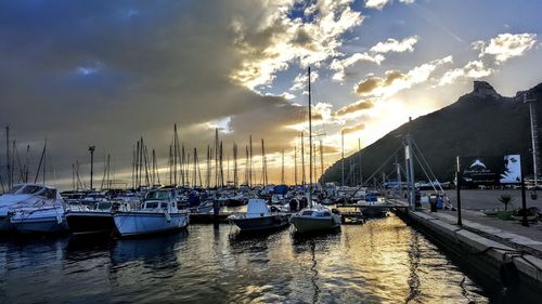 Boats moored in harbor at sunset