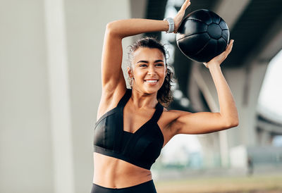 Smiling young woman exercising with ball while standing outdoors