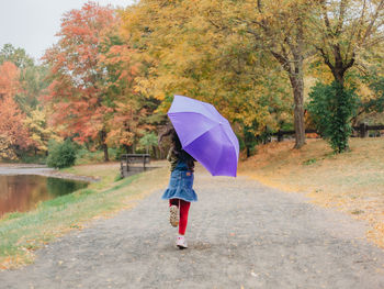 Woman with umbrella walking on wet road during rainy season