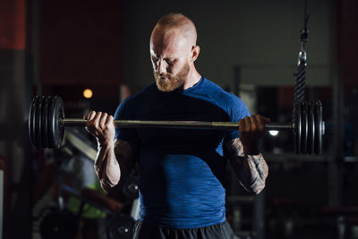 Mid adult sportsman lifting barbell while standing in gym