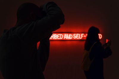 Rear view of man and woman standing against illuminated sign