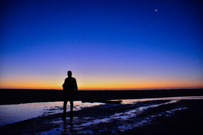 Silhouette man standing on shore against sky during sunset