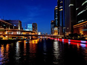 Illuminated bridge over river by buildings against sky at dusk