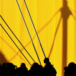 Silhouette people standing against yellow wall during sunny day
