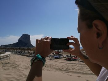 Cropped image of woman photographing rock formation on beach at calpe