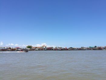 Sea by cityscape against clear blue sky