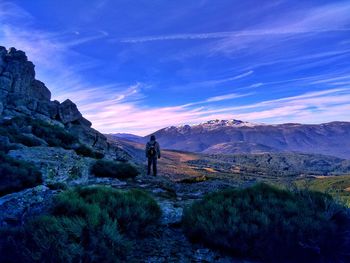 Man standing on mountain against blue sky and sunset colored clouds