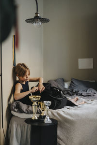 Elementary boy packing backpack while sitting on bed in bedroom