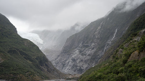 Wide shot of massive glacier flowing into a valley through steep rock walls shot in new zealand