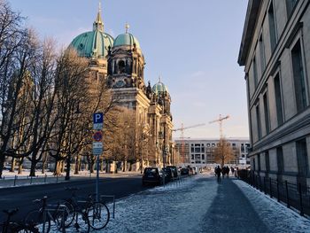 Snowy street by berlin cathedral against sky in city