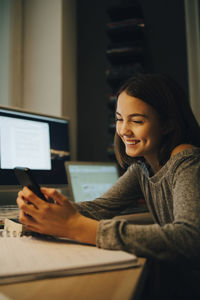 Smiling girl using smart phone while sitting at desk