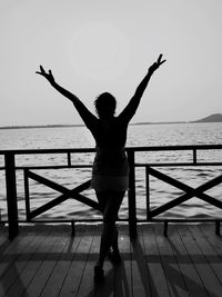 Rear view of woman with arms outstretched while standing by railing against sea