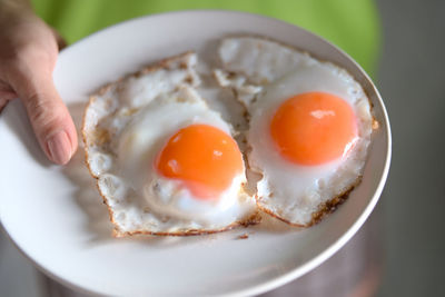 Cropped image of woman holding plate with fried eggs