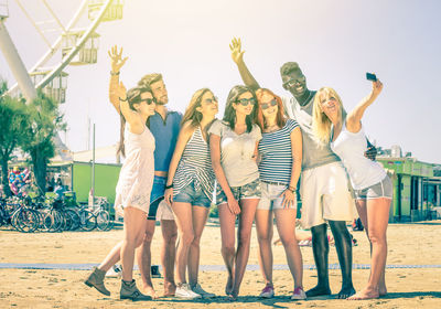 Happy friends taking selfie while standing at beach during sunny day