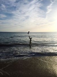 Father tossing baby in mid-air at beach against sky