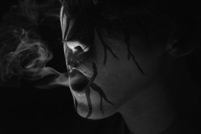Close-up of young woman smoking over black background