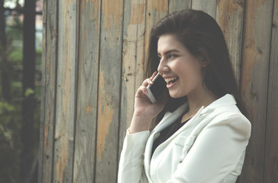 Portrait of young woman using phone while standing on wood