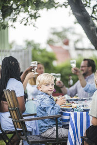 Boy having drink while sitting in chair at garden party with friends and family