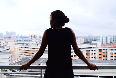 Rear view of woman looking through window in city