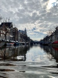 Sailboats moored on river by buildings against sky