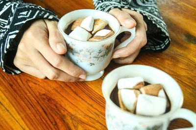 Close up of hands holding a cup of hot chocolate drink with marshmallows on a christmas morning