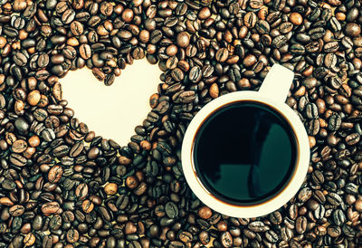 Close-up of coffee cup by heart shape amidst roasted beans