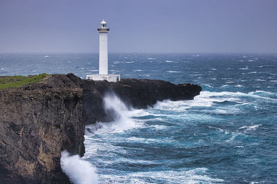 Lighthouse by sea against clear blue sky