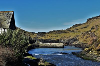 Scenic view of river by mountains against clear blue sky