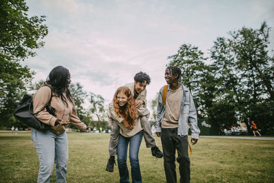 Playful teenage girl piggybacking male friend at park
