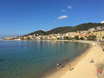 People on beach by buildings against blue sky