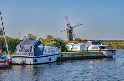  boats moored up on river bank in the countryside with a windmill in the distance