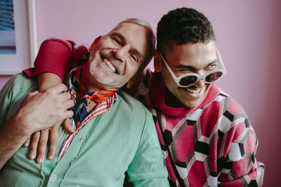 Happy gay man with arm around mature friend at home