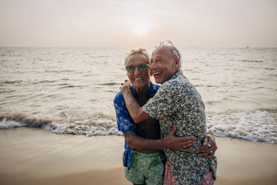 Cheerful senior gay couple embracing each other on vacation at beach