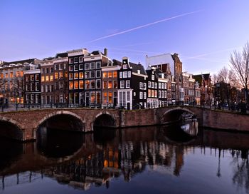 Reflection of bridge in river against clear sky